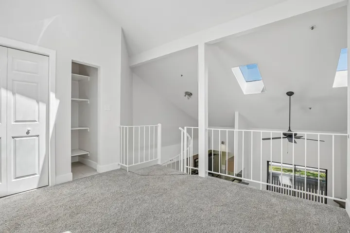 Loft area featuring vaulted ceilings, two skylights, a ceiling fan, and white railing overlooking the lower level
