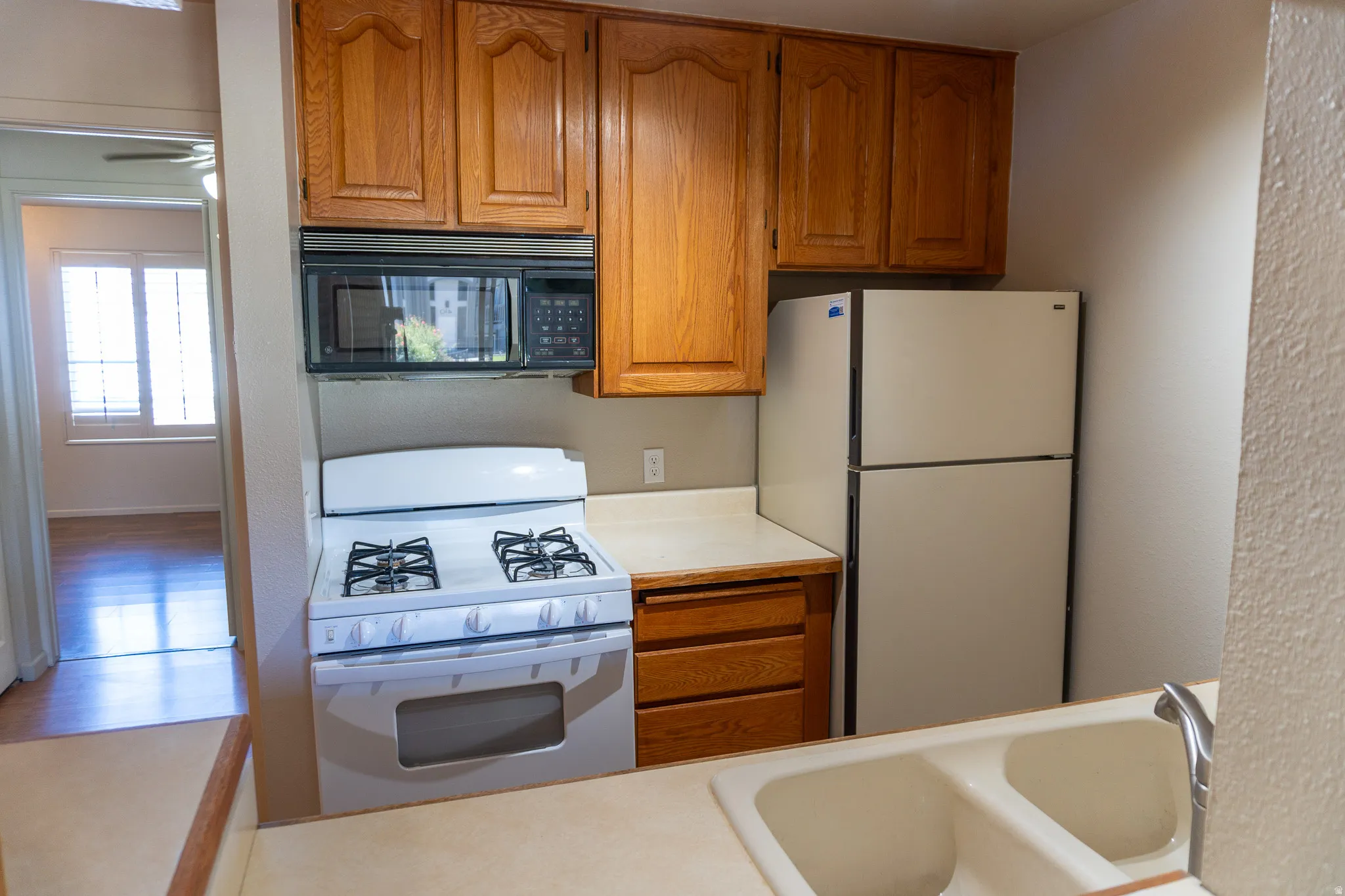 Kitchen featuring wood cabinetry, white appliances, a gas range with an overhead microwave, and a double basin sink