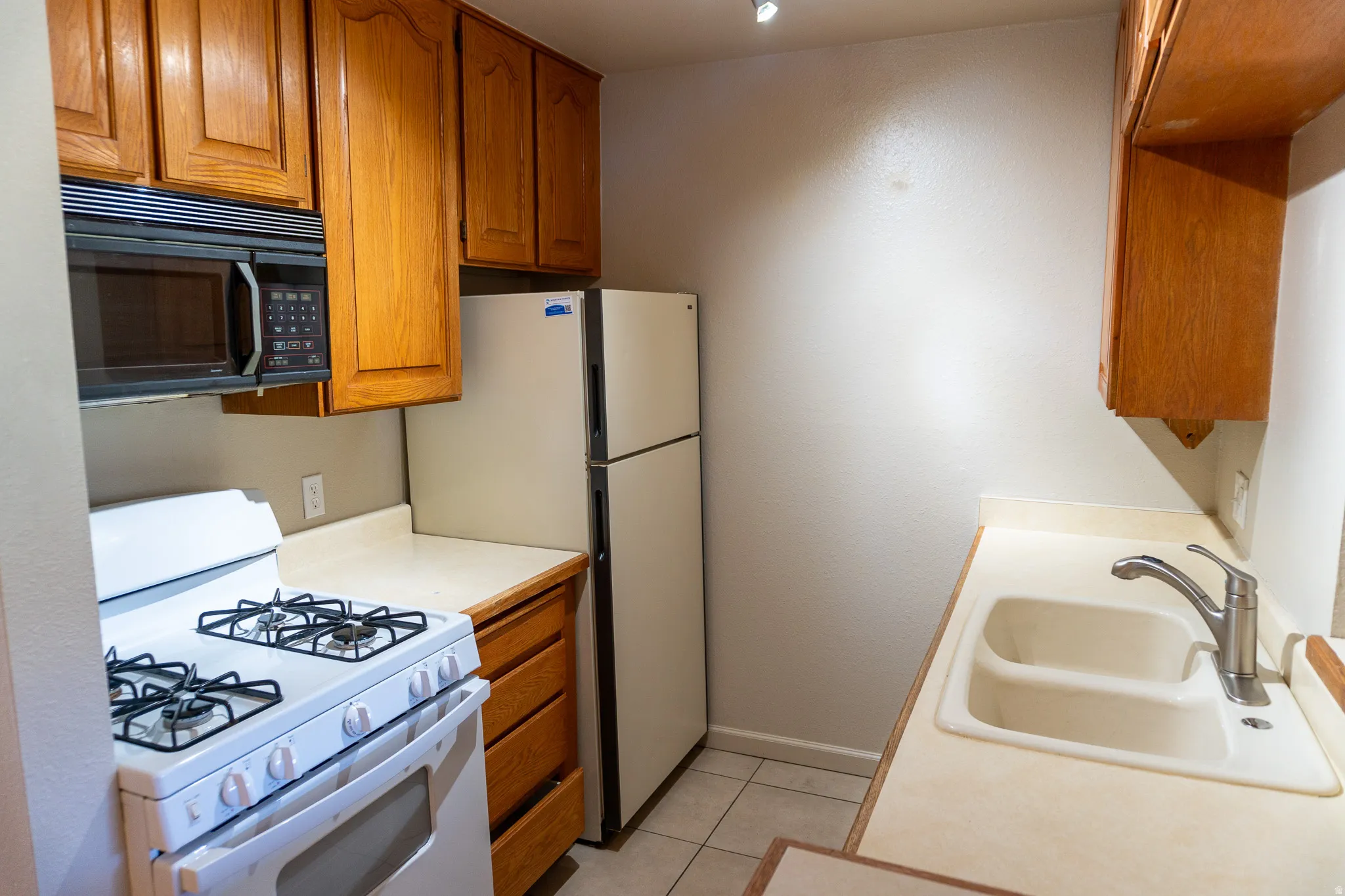 Kitchen featuring wood cabinetry, a built-in microwave, gas range, and double basin sink with a chrome faucet