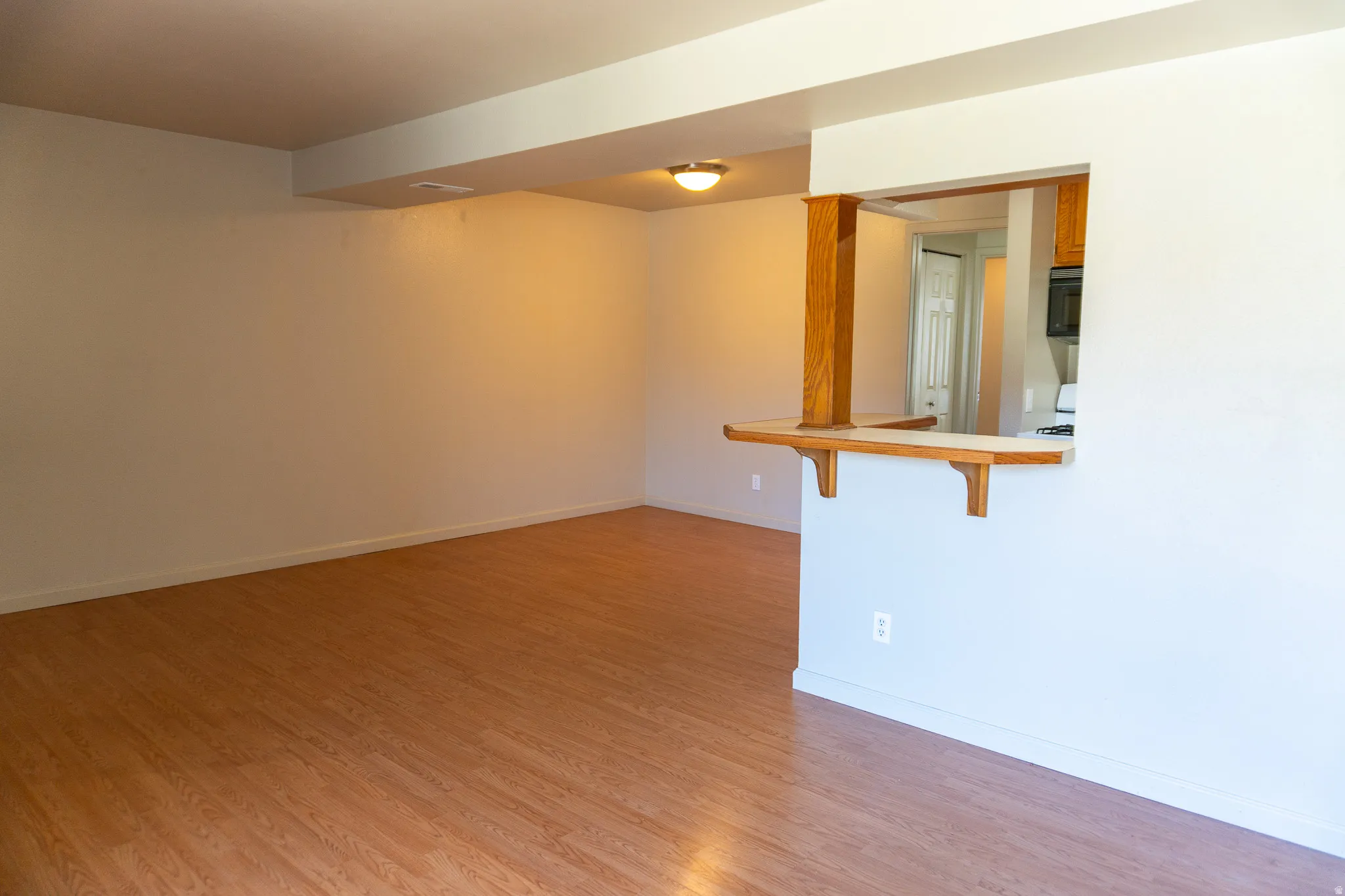 Spacious room featuring wood-finish flooring, light-toned walls, and a pass-through opening with a wood-accented breakfast bar