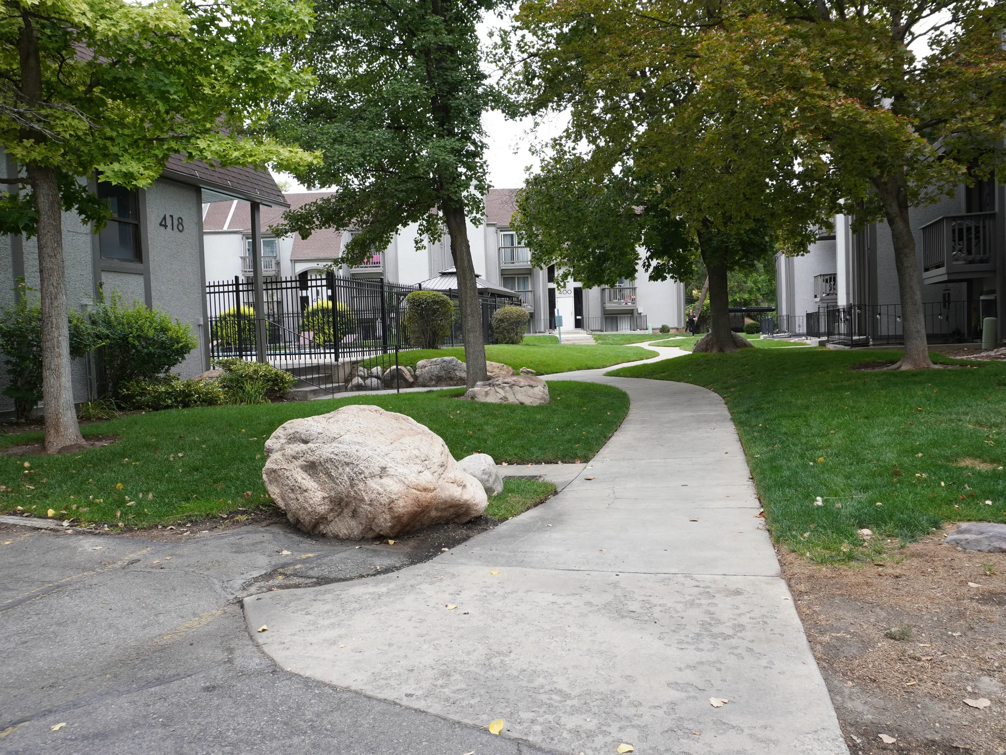 Landscaped grounds featuring a winding concrete pathway, mature trees, and natural rock accents