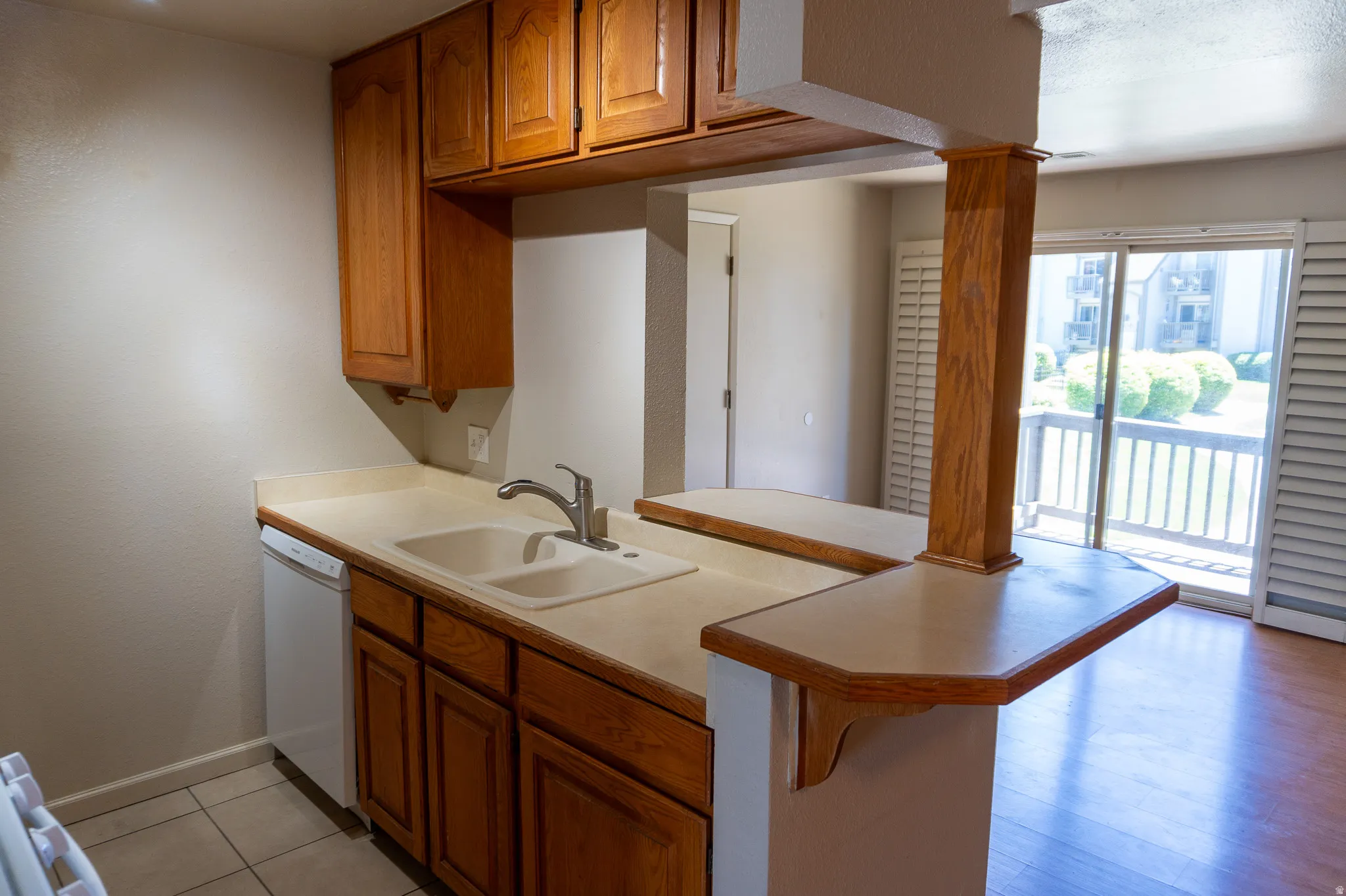 Kitchen area featuring wood cabinetry, a double basin sink with a gooseneck faucet, light-toned countertops, and a breakfast bar