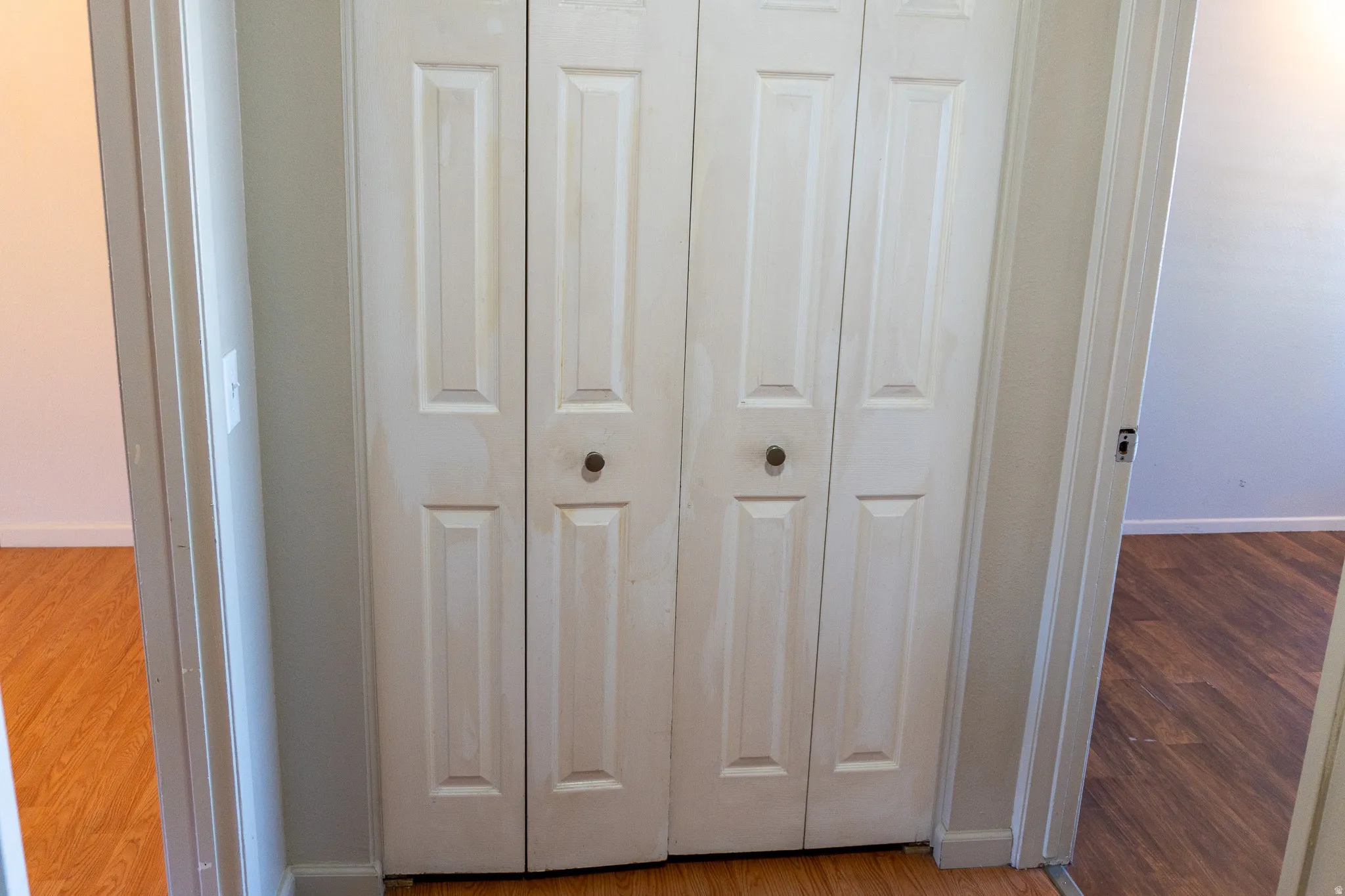 White bi-fold closet doors with round hardware, framed by neutral painted walls and wood-finish flooring