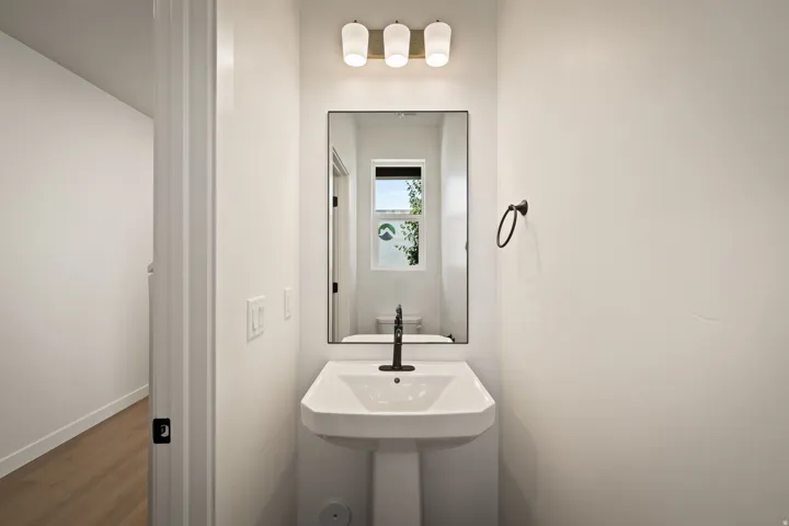 Pedestal sink with black wall-mounted faucet, rectangular mirror, and three-light vanity fixture