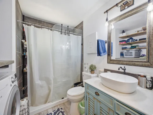 Bathroom featuring a shower with dark tiled surround, a white vessel sink, a distressed-finish vanity, and a large framed mirror