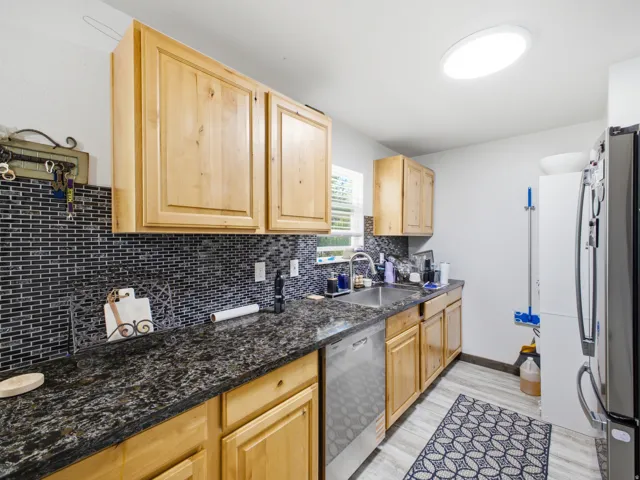 Kitchen featuring light wood cabinetry, dark speckled countertops, and a full-height dark mosaic tile backsplash