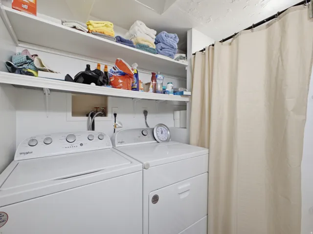Dedicated utility area with stacked shelving, white appliances, and a privacy curtain