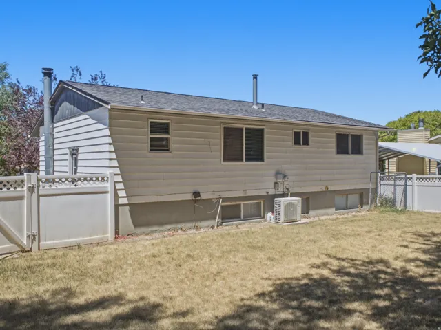 Rear exterior featuring horizontal siding, multiple windows, a grey shingle roof, and a white fence