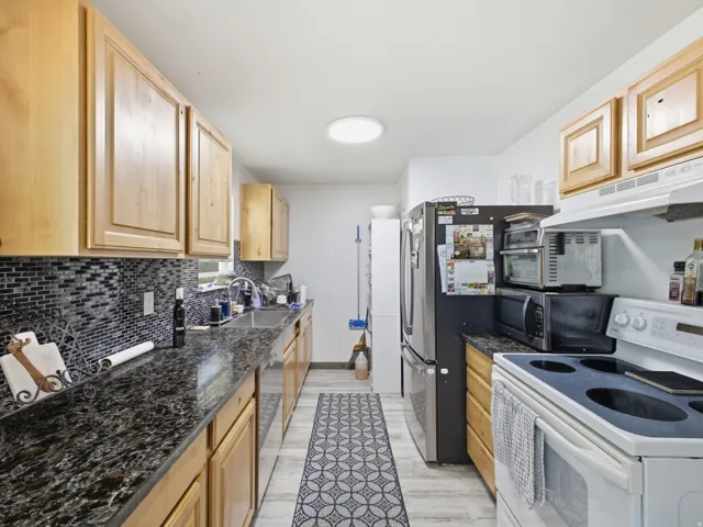 Galley kitchen featuring light wood cabinetry, dark speckled countertops, and a mosaic tile backsplash