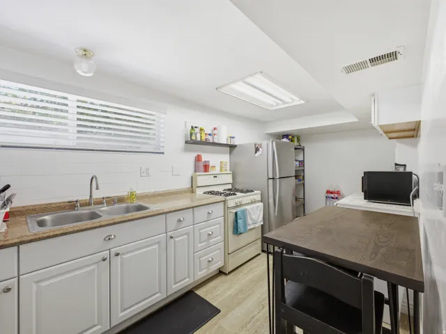 Kitchen featuring white cabinetry, granite-style countertops, a double basin stainless steel sink, a gas range, and wood-finish flooring