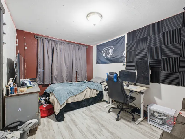 Bedroom featuring light wood-finish flooring, a red accent wall, and a full-wall acoustic panel installation