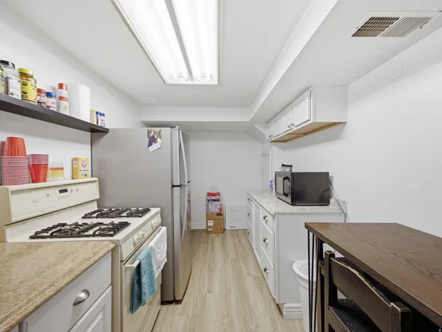 Compact kitchen featuring a full-size stainless steel refrigerator, white gas range, and built-in upper cabinetry