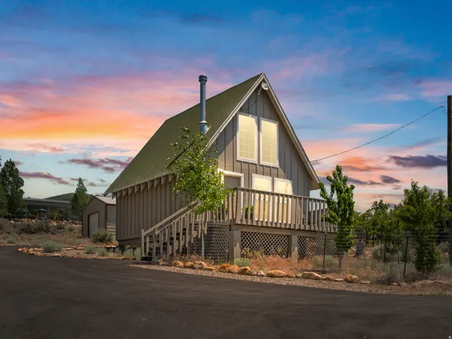 Cabin with a green asphalt shingle roof, a front-facing deck with wooden railing and lattice skirting, and an asphalt driveway