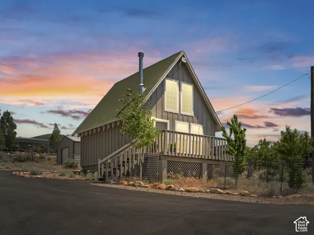Cabin with a green asphalt shingle roof, a front-facing deck with wooden railing and lattice skirting, and an asphalt driveway