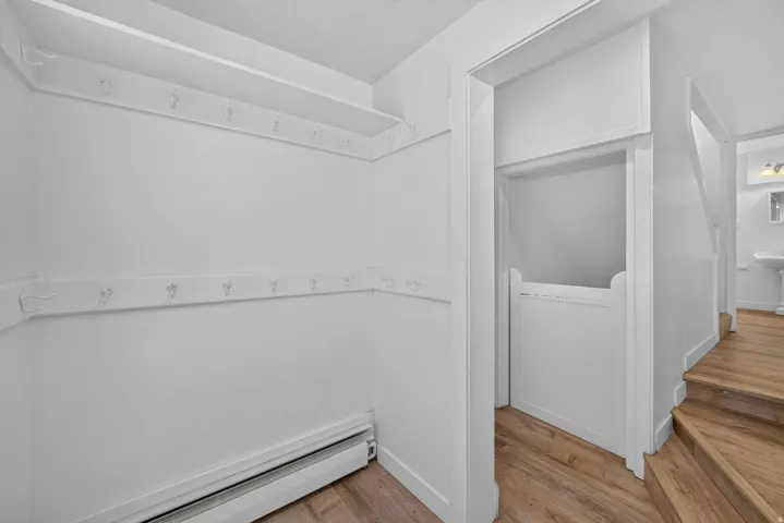 Entryway featuring wood-finish flooring, white walls, and built-in coat hooks with an overhead shelf