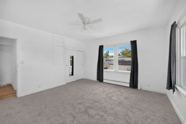 Carpeted room featuring multiple windows with dark curtains, a ceiling fan, and white walls