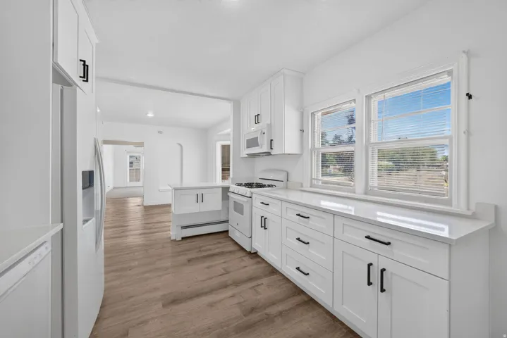Contemporary kitchen featuring white shaker cabinetry, quartz countertops, white appliances, and wood-finish flooring