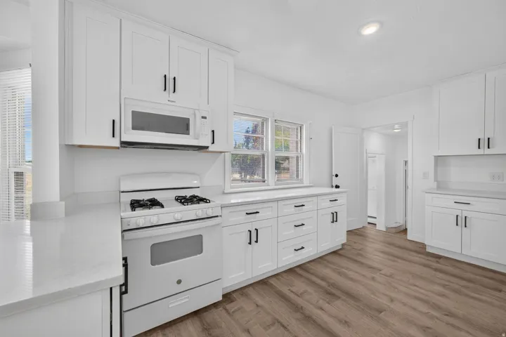 Modern kitchen featuring white shaker cabinetry, quartz countertops, stainless steel appliances, and wood-finish flooring
