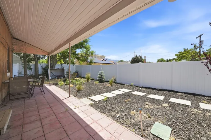 Covered patio with red tile flooring, featuring a white vinyl fence and a landscaped garden bed with stepping stones