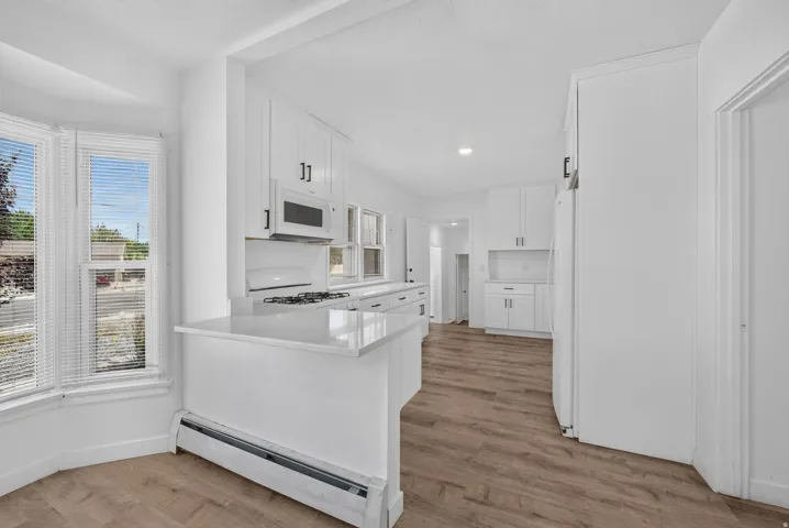 Bright kitchen featuring white cabinetry, light-toned wood-finish flooring, and white countertops