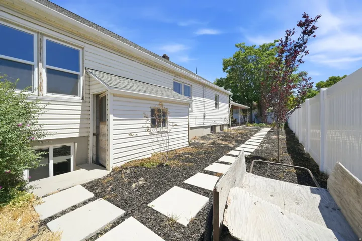 Side yard featuring concrete stepping stones, dark ground cover, a young tree with red foliage, and white vinyl fencing