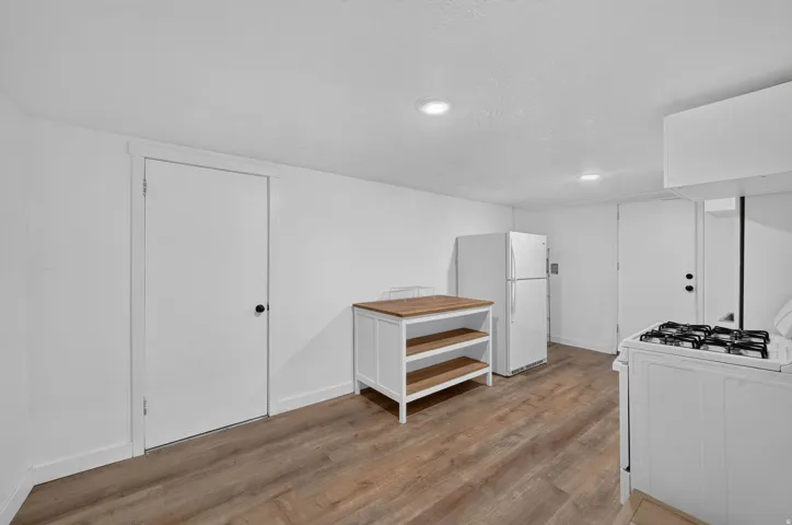 Contemporary kitchen featuring wood-finish flooring, white walls, recessed lighting, and a white gas range with a matching hood