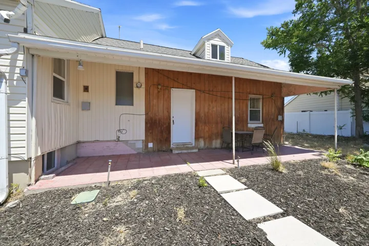 Covered patio with a red paver surface, wood-paneled exterior siding, and a white entry door