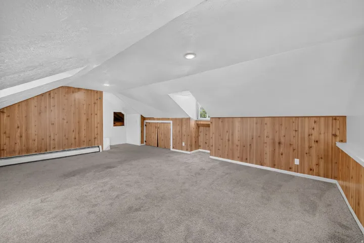 Carpeted room featuring wood paneling, sloped ceilings, recessed lighting, and built-in storage closets