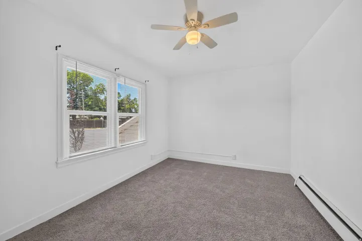 Bright room featuring a multi-pane window with blinds, a ceiling fan with integrated lighting, and plush grey carpeting