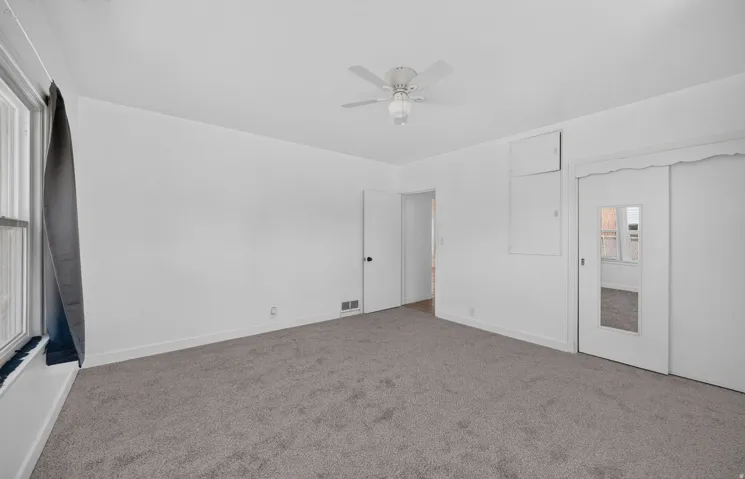 Spacious interior room featuring gray carpet flooring, white walls, and a ceiling fan with integrated lighting