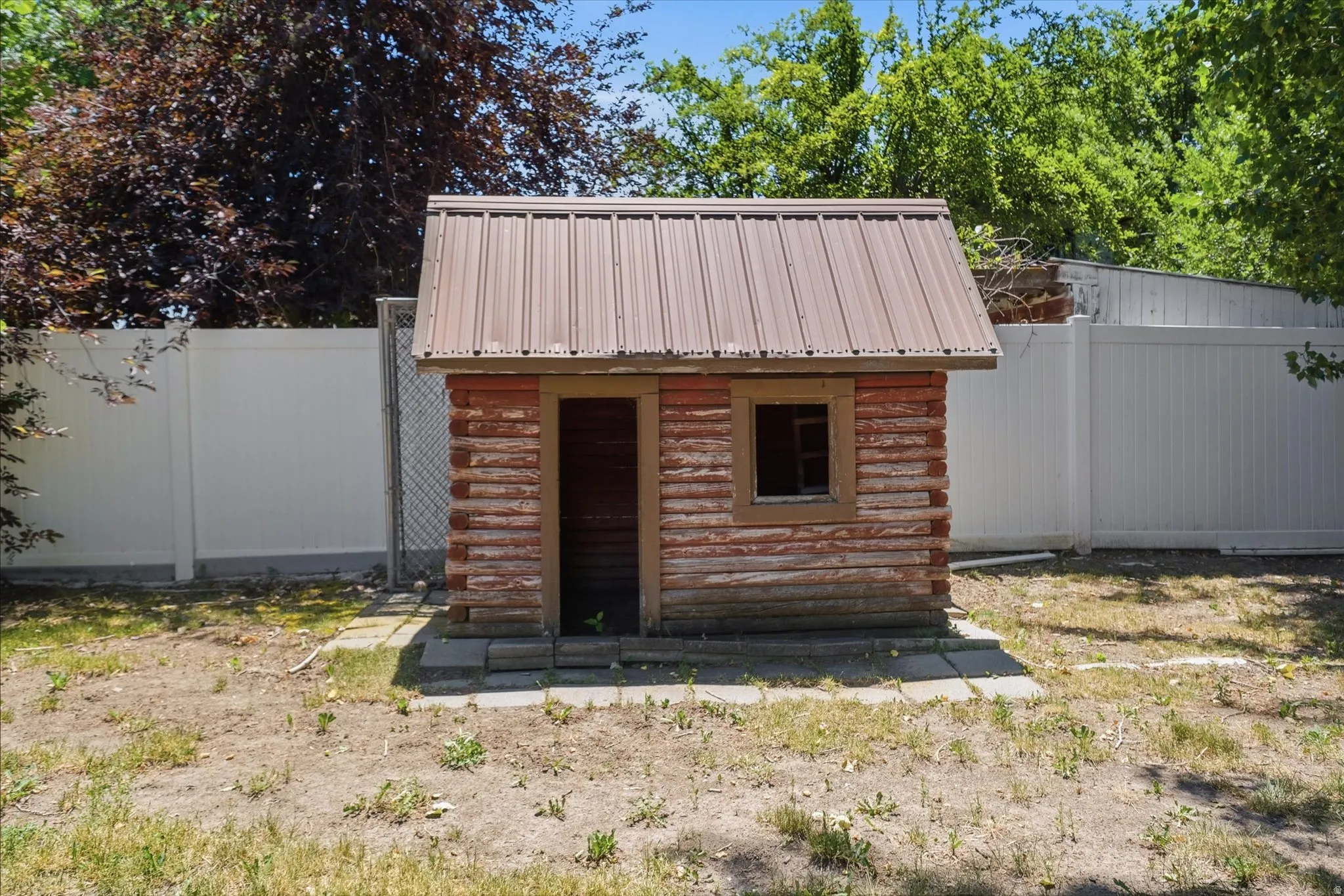 Rustic wood shed with a metal roof, featuring a small window opening and a wooden door frame, set on a stone paver base
