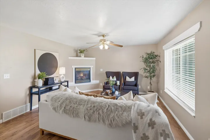 Spacious living area featuring wood-finish flooring, a corner fireplace with a white mantel, and a ceiling fan