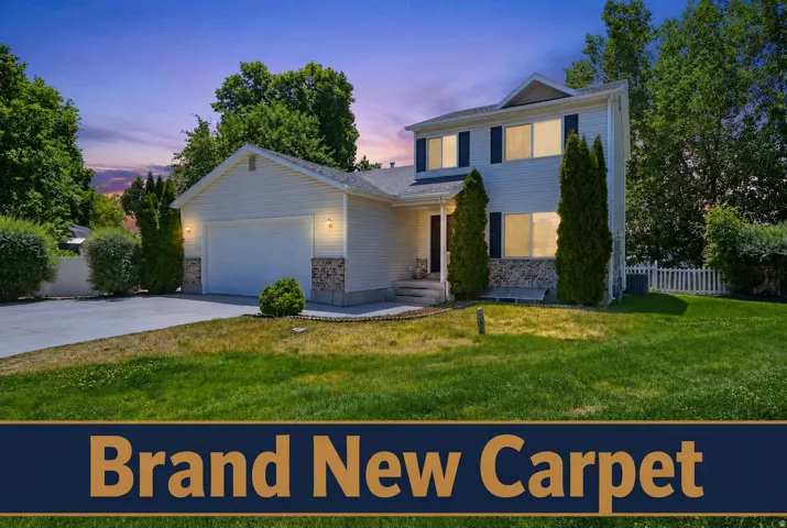 Two-story colonial home featuring a white fiber cement exterior, attached two-car garage with white panel doors, and manicured front lawn bordered by mature evergreen landscaping