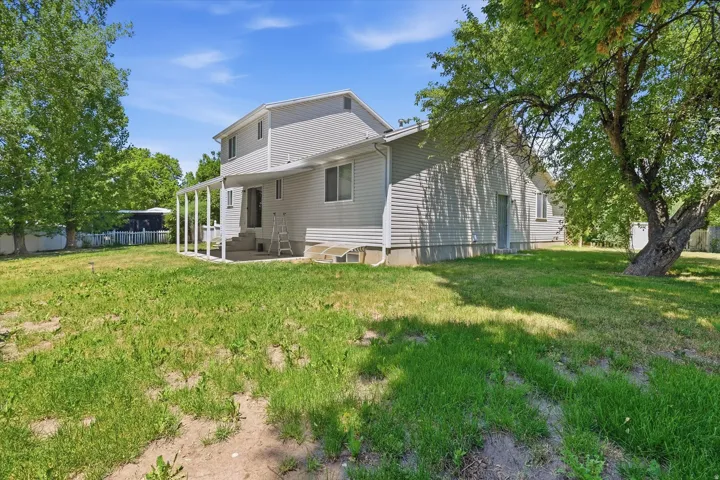 Spacious backyard featuring a covered patio, mature trees, and a perimeter fence