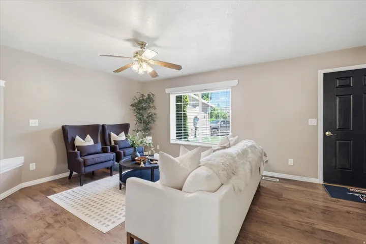 Spacious living area featuring wood-finish flooring, a ceiling fan with integrated lighting, and neutral wall tones