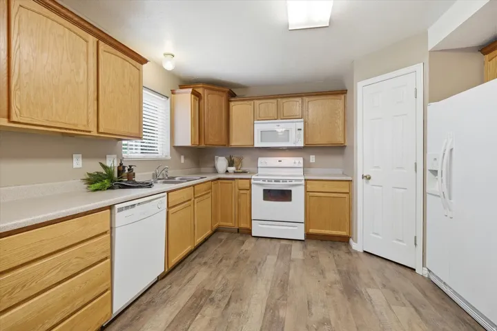 Kitchen featuring wood-finish cabinetry, light-toned countertops, white appliances, and wood-look flooring