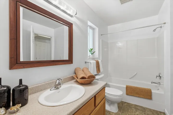 Bathroom featuring a wood-finish framed mirror, a vanity with an integrated sink, a full bathtub with a shower, a toilet, and a window for natural light