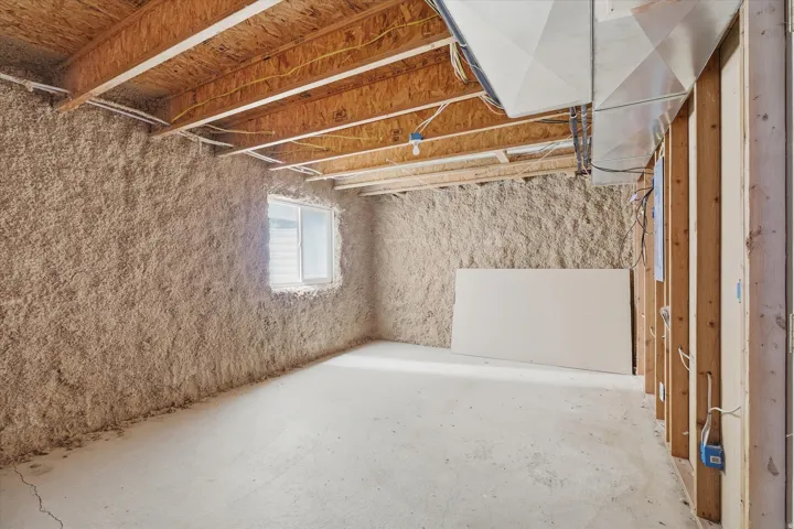 Unfinished basement space featuring exposed wood joists, concrete flooring, and a single window
