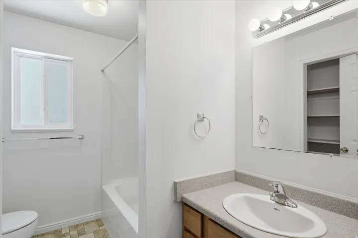 Bathroom featuring a vanity with an integrated sink, a large mirror with a four-bulb light fixture, a shower-tub combination, and a window with privacy glass