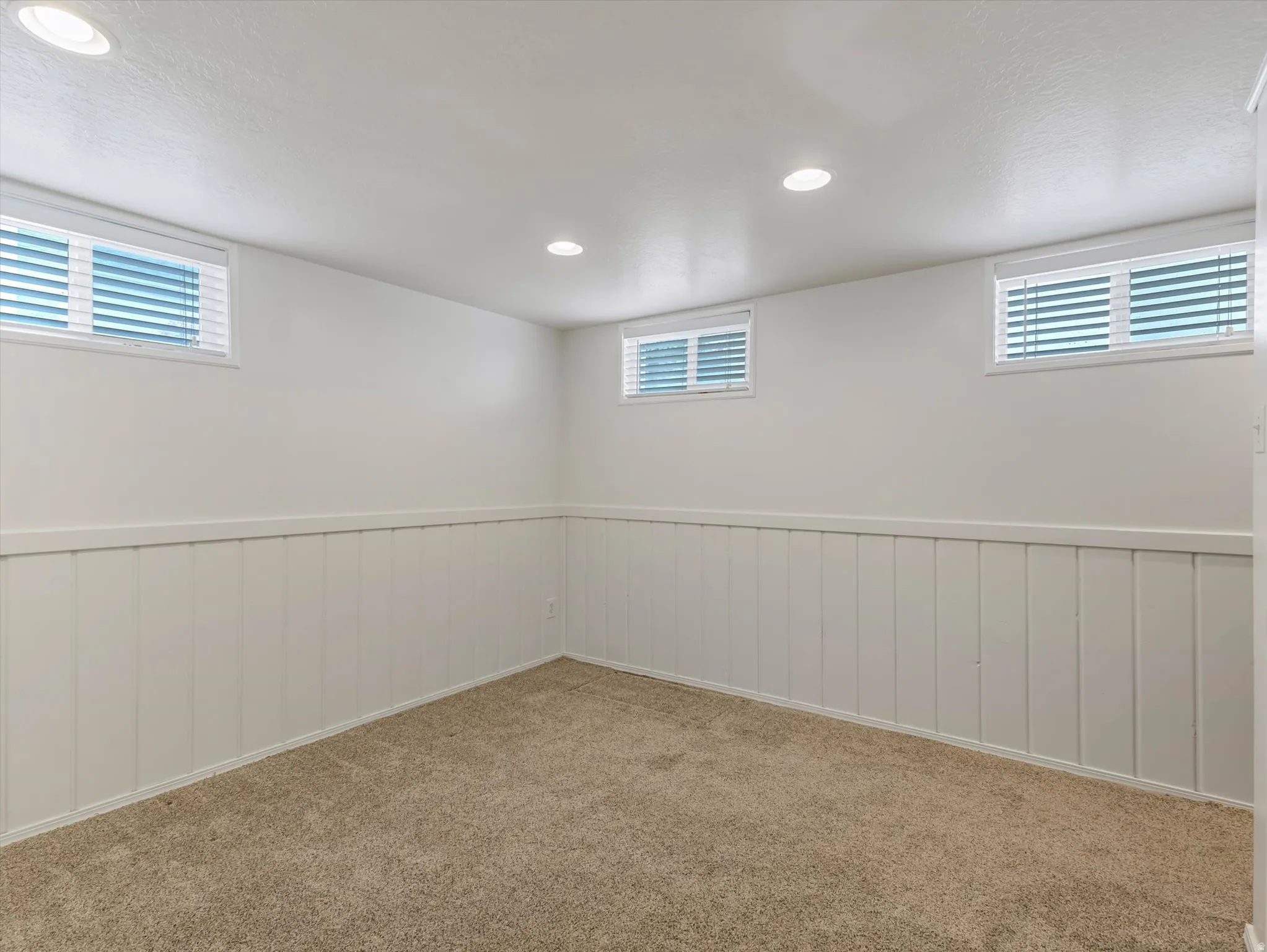 Carpeted room featuring white board and batten wainscoting, light-toned walls, recessed ceiling lighting, and multiple horizontal windows with blinds