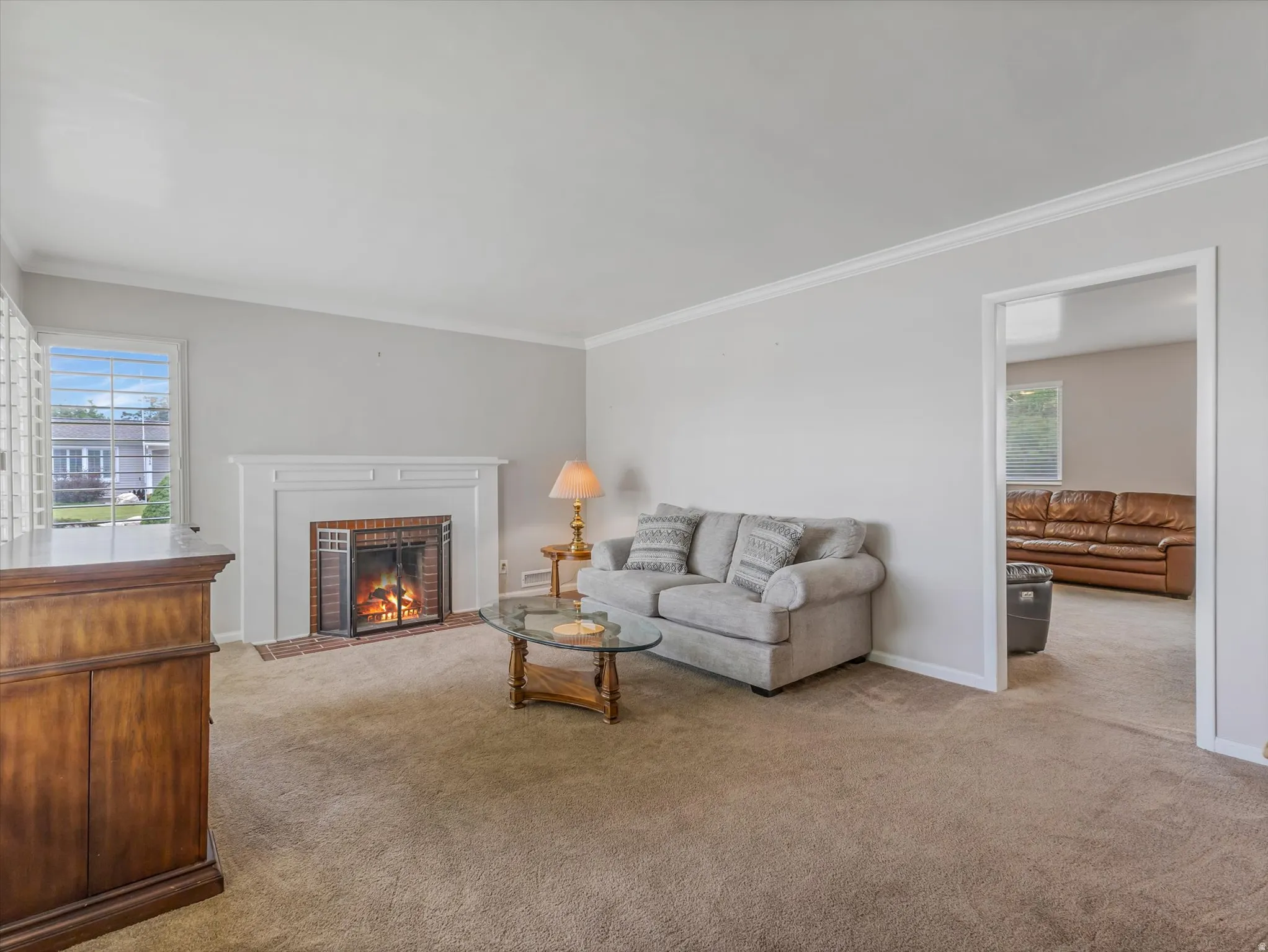 Living area featuring a white mantelpiece with a brick hearth and firebox, carpet flooring, and white trim