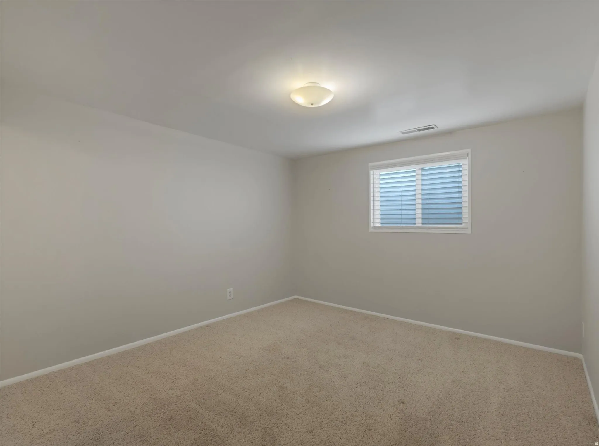 Carpeted room featuring a single window with horizontal blinds, neutral wall paint, white trim, and a ceiling-mounted light fixture