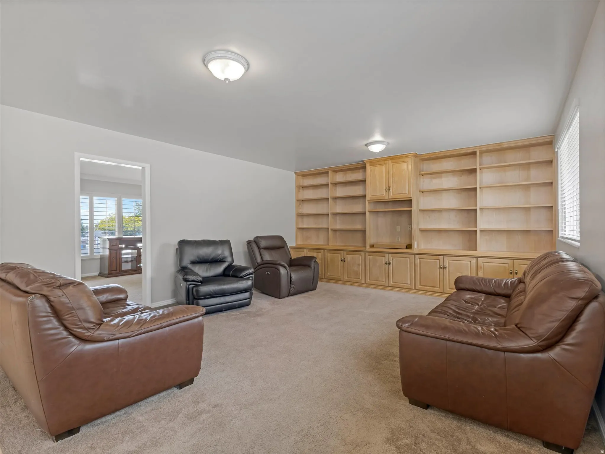 Room featuring an extensive built-in wooden shelving unit with integrated cabinetry, complemented by neutral carpeting and light-toned walls