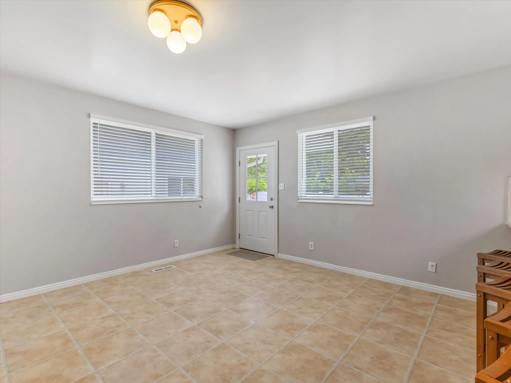 Light-filled room featuring large windows with blinds, a side entry door, and durable tile flooring