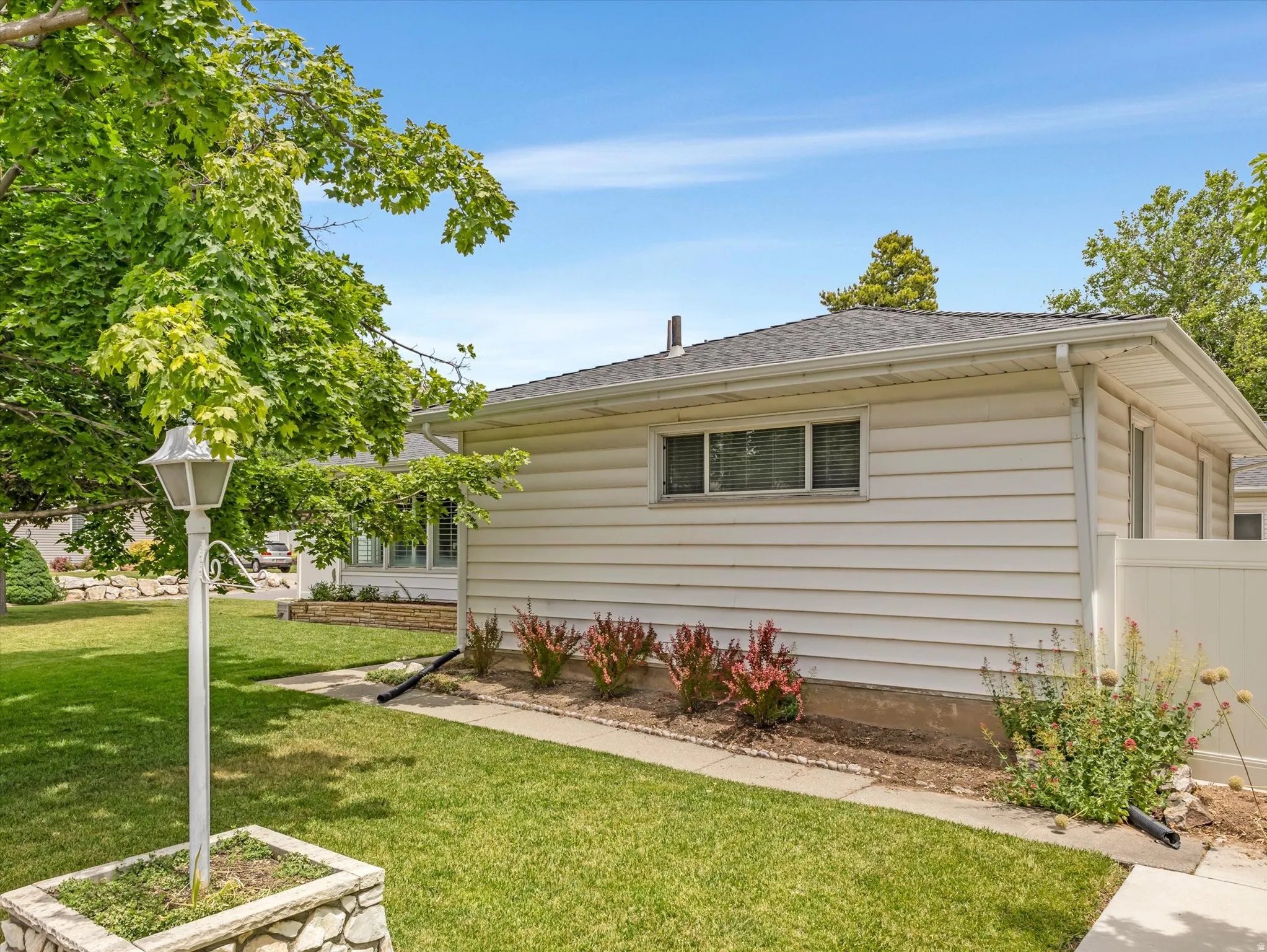White horizontal siding exterior with a dark shingle roof, featuring a concrete walkway, established green lawn, and decorative landscaping