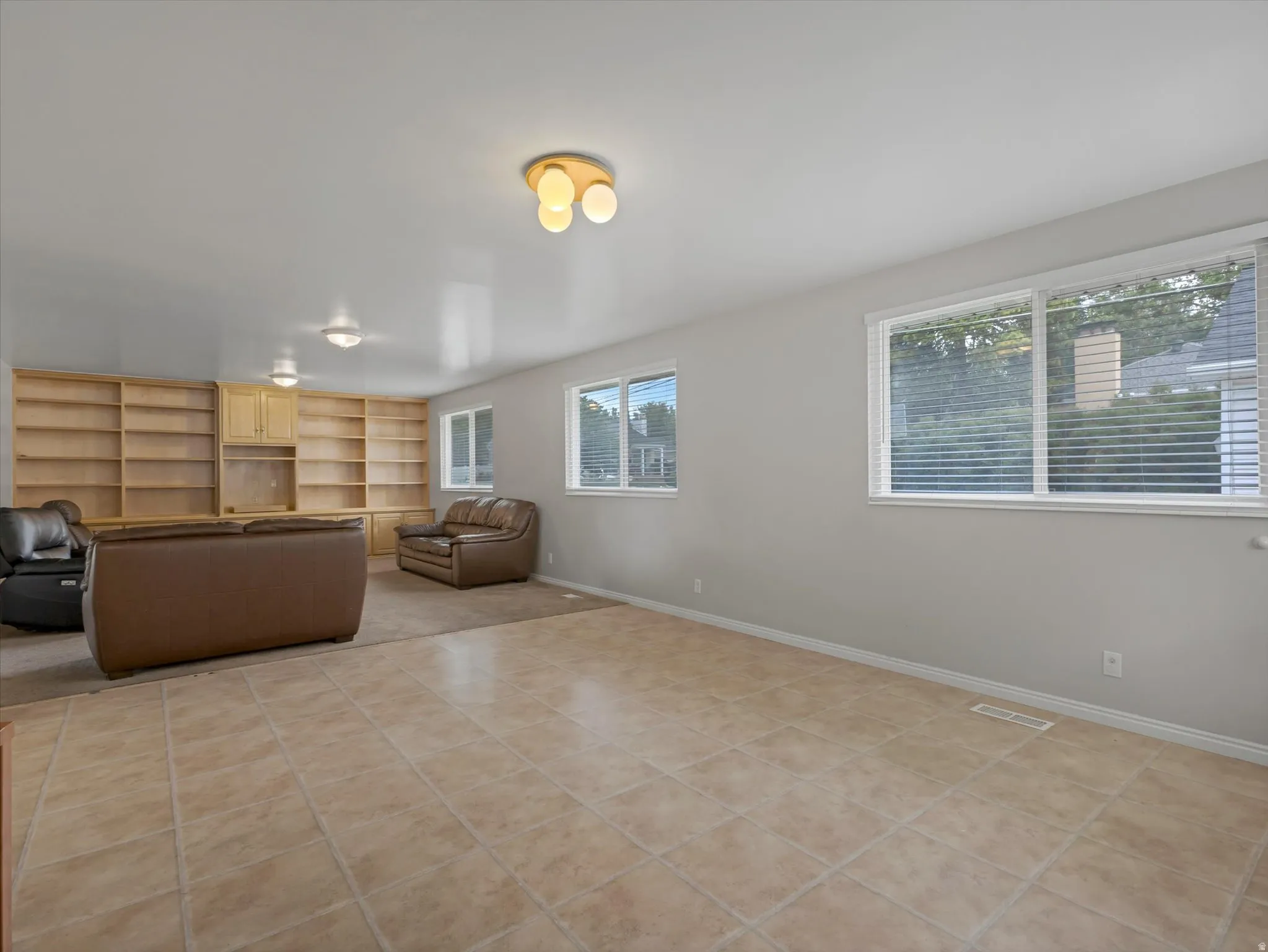 Open living area featuring light-toned square floor tiling and an integrated carpeted section