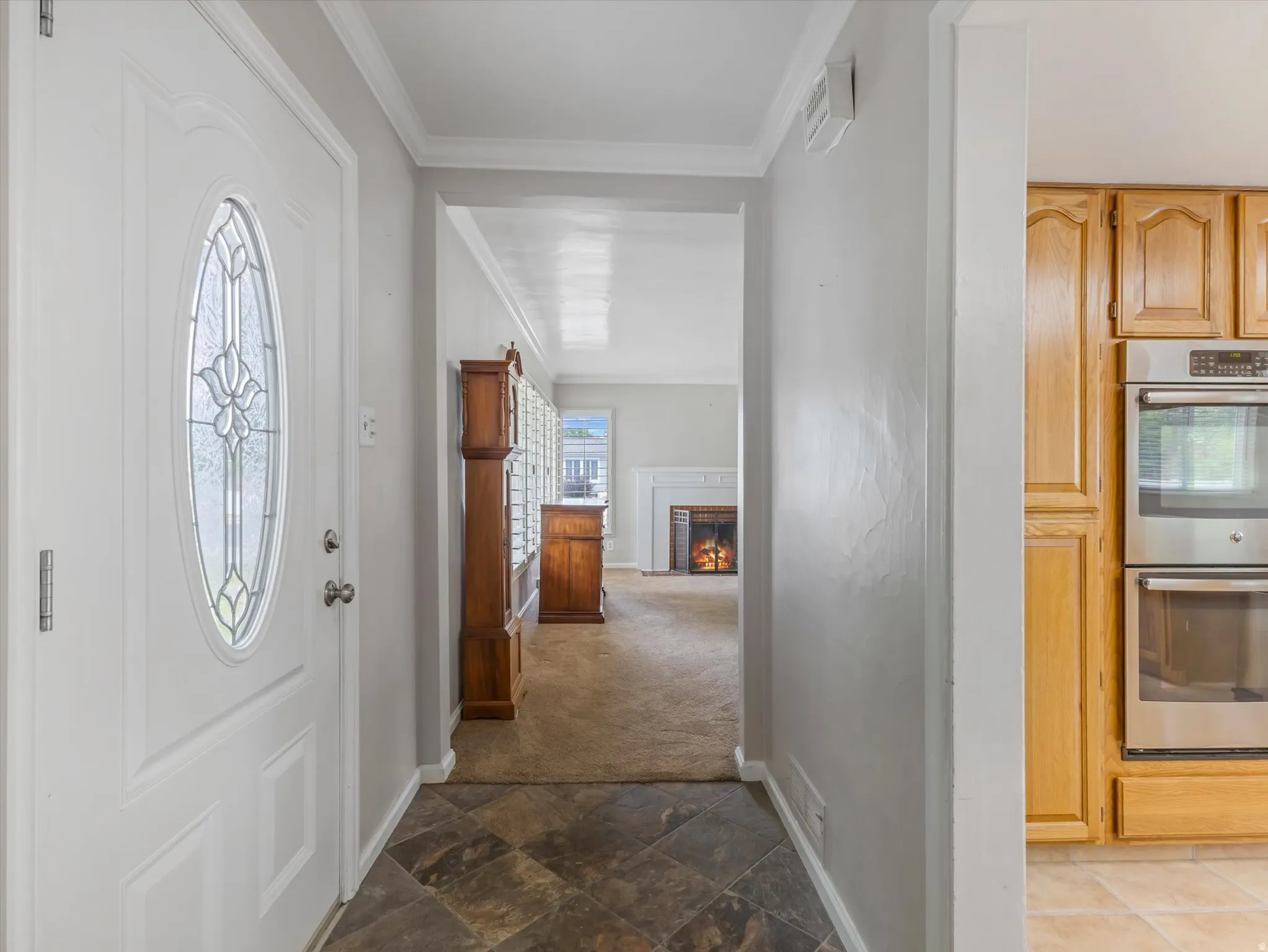 Entryway featuring a white door with an oval decorative glass insert, slate-finish floor tile, and crown molding
