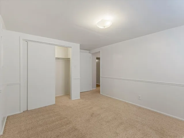 Spacious room featuring neutral carpeting, white walls with chair rail molding, a flush-mount ceiling light fixture, and a closet with sliding doors