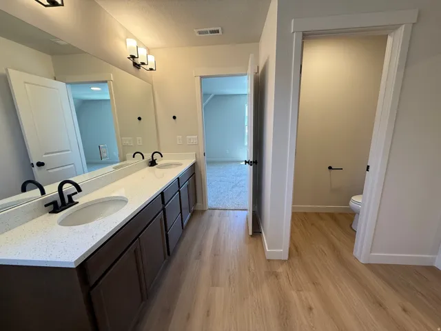 Dual undermount sinks with matte black fixtures set into a speckled white countertop, framed by a full-width mirror and contemporary vanity lighting