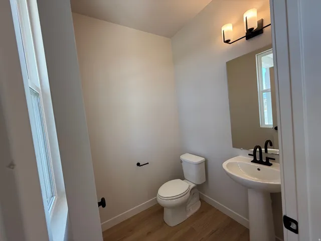 Powder room featuring a pedestal sink with a matte black faucet, a rectangular wall-mounted mirror, and a two-bulb vanity light fixture